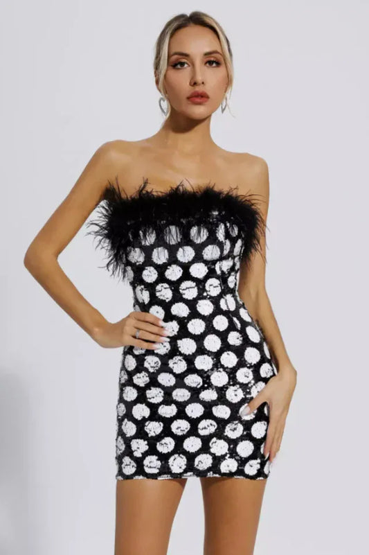 Woman wearing a black and white polka dot sequin strapless mini dress with black feather trim