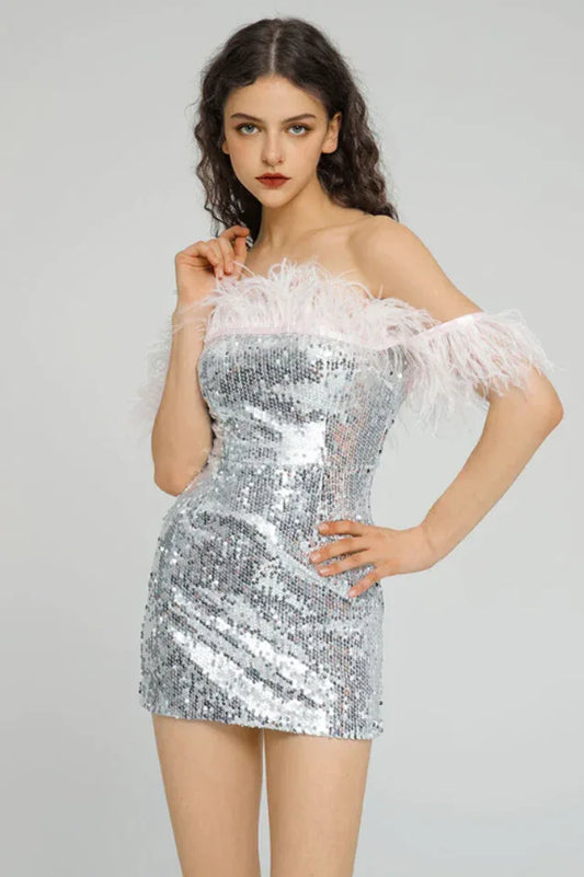 Model wearing a silver sequined off-the-shoulder dress with feather trim, posing with her hand on her hip.