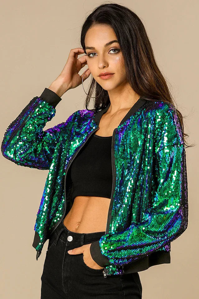 Front view of a woman in a sequined bomber jacket and black jeans, hands in pockets.