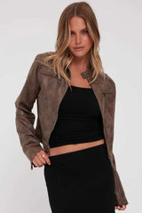 Woman wearing a brown faux leather cropped jacket with a black tank top and black skirt, front view.