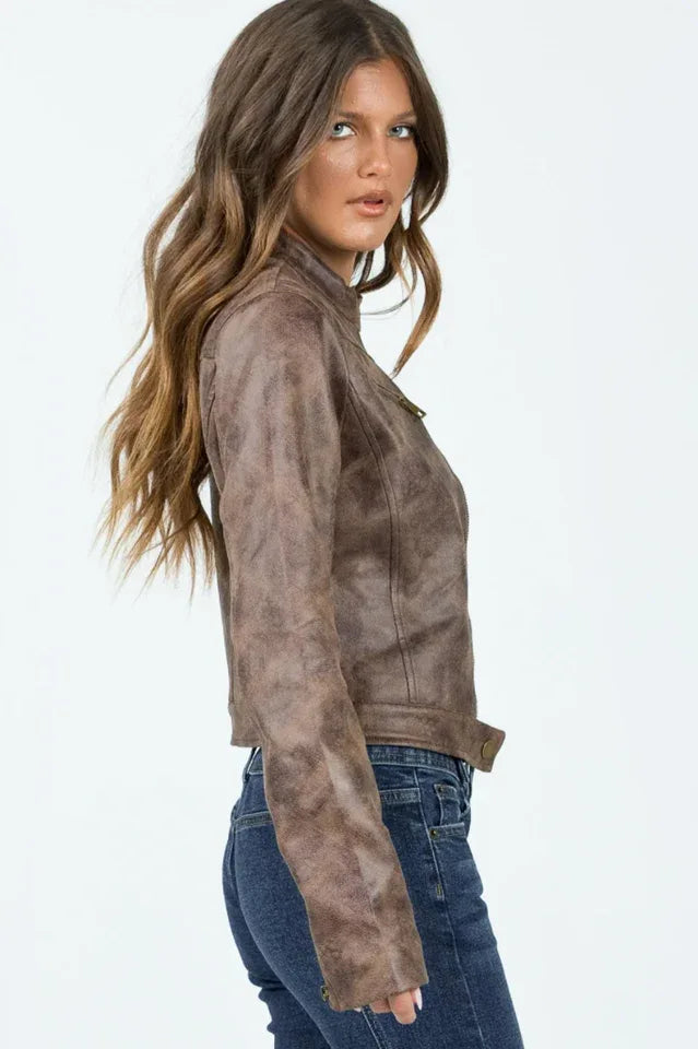 Woman wearing a brown faux leather cropped jacket with a white tank top and blue jeans, side view.