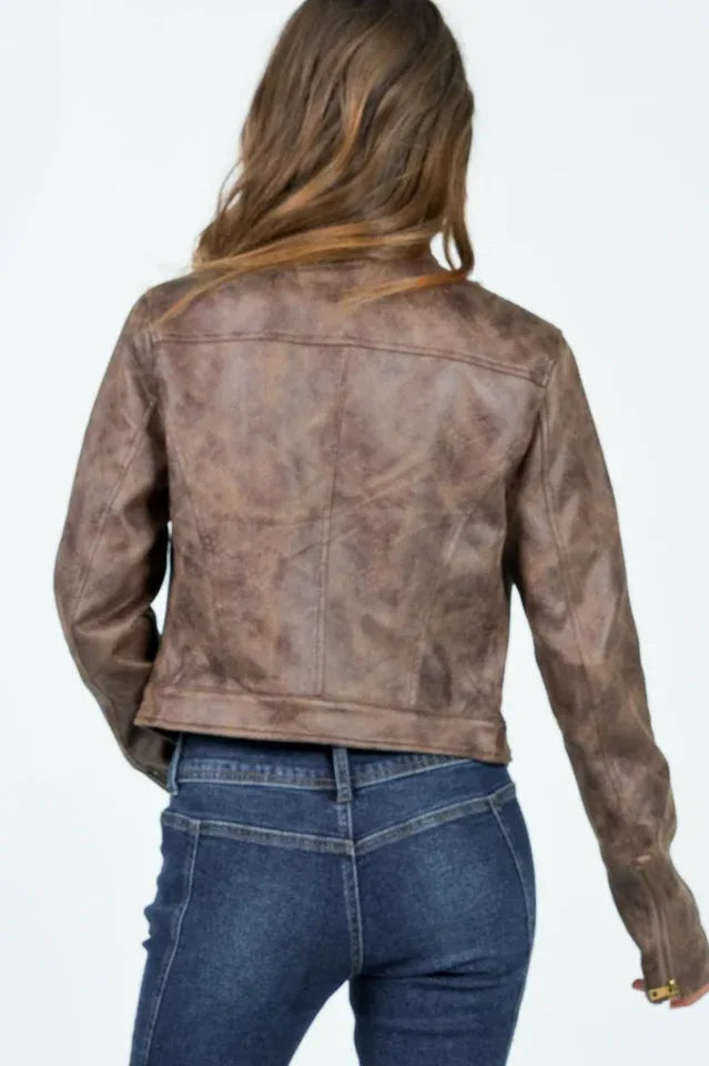 Woman wearing a brown faux leather cropped jacket with a white tank top and blue jeans, back view.