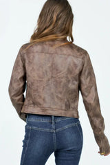 Woman wearing a brown faux leather cropped jacket with a white tank top and blue jeans, back view.