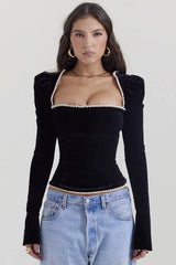 Model wearing a black velvet long-sleeve top with a square neckline and puffed shoulders, paired with light-wash denim jeans.
