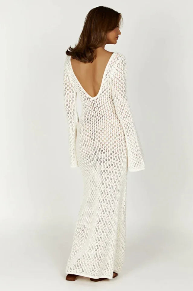 Woman wearing a long white crochet knit dress with bell sleeves and a deep V-neckline, back view