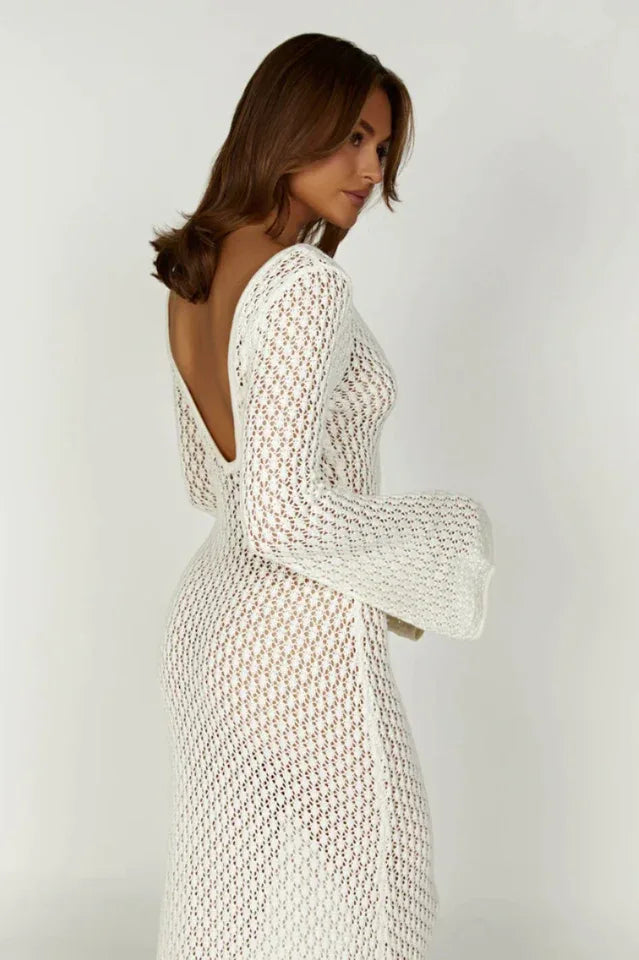 Woman wearing a long white crochet knit dress with bell sleeves and a deep V-neckline, side profile
