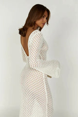 Woman wearing a long white crochet knit dress with bell sleeves and a deep V-neckline, side profile