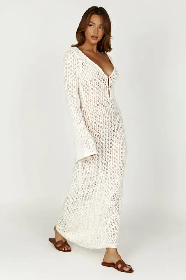 Woman wearing a long white crochet knit dress with bell sleeves and a deep V-neckline, side view