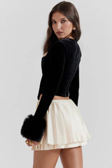 Rear view of a woman wearing a black velvet top with faux fur cuffs and a cream pleated mini skirt.