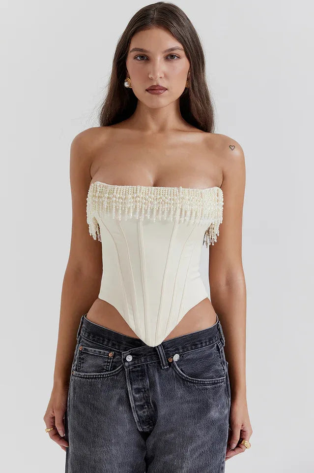 Model wearing a cream strapless corset top with beaded fringe detail and dark wash jeans.