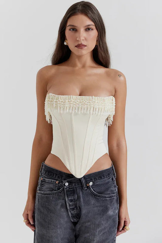 Model wearing a cream strapless corset top with beaded fringe detail and dark wash jeans.