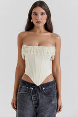 Model wearing a cream strapless corset top with beaded fringe detail and dark wash jeans.