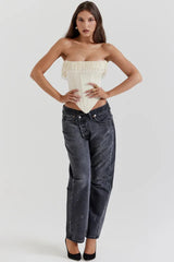 Model posing with hands on hips, wearing a cream strapless corset top with beaded fringe detail and dark wash jeans, paired with black heels.