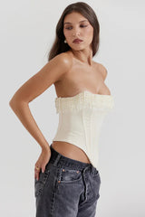 Side view of a model in a cream strapless corset top with beaded fringe detail and dark wash jeans.