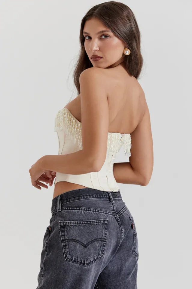 Rear view of a model wearing a cream strapless corset top with beaded fringe detail and dark wash jeans.