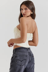 Rear view of a model wearing a cream strapless corset top with beaded fringe detail and dark wash jeans.