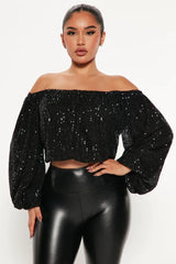 Woman wearing a black sequined off-the-shoulder top with balloon sleeves and black leather pants, front view
