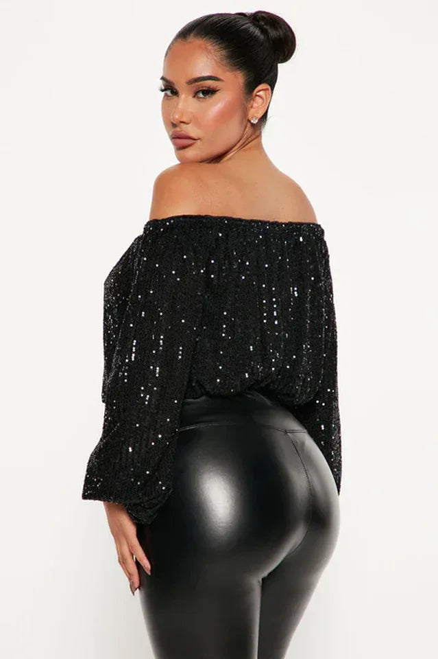 Woman wearing a black sequined off-the-shoulder top with balloon sleeves and black leather pants, back view