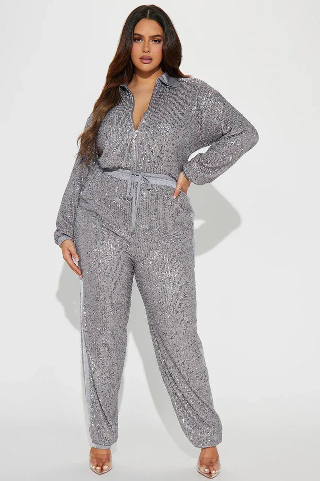 Woman wearing a grey sequined long-sleeved collared jumpsuit with a zipper front closure and drawstring waist. The pants have a grey side stripe.