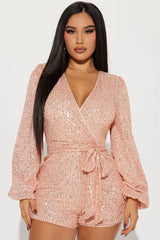 woman wearing a pink sequin romper with long puffed sleeves and a tie waist