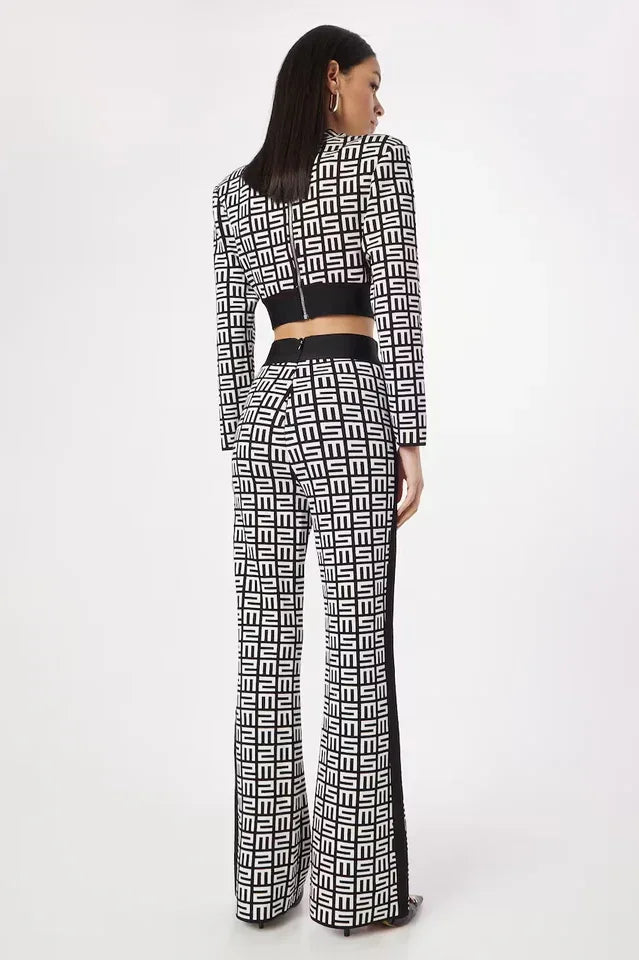 Back view of a woman wearing a black and white monogram print knit cropped long sleeve top with shoulder pads and matching flare pants with a contrasting side stripe