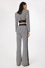 Back view of a woman wearing a black and white monogram print knit cropped long sleeve top with shoulder pads and matching flare pants with a contrasting side stripe
