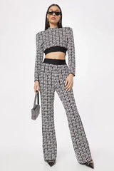 Woman wearing a black and white monogram print knit cropped long sleeve top with shoulder pads and matching flare pants with a contrasting side stripe, holding a small black embellished handbag