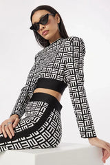 Close-up of a woman wearing a black and white monogram print knit cropped long sleeve top with shoulder pads and matching flare pants, accessorized with cat-eye sunglasses and hoop earrings