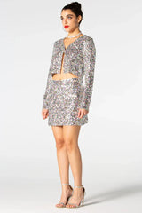 Woman wearing a sequined cropped jacket and matching mini skirt, side view