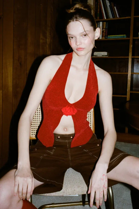 Model wearing a red halter top and brown shorts sitting on a chair.