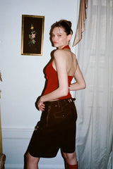 Model wearing a red halter top and brown shorts standing against a wall, showing the back of the top.