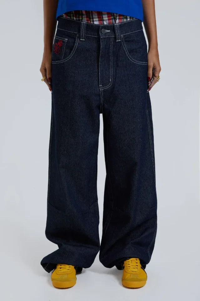 Close-up of woman's legs wearing dark wash wide leg jeans with plaid waistband detail and yellow shoes