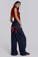Woman from the back wearing dark wash wide leg jeans with embroidered logo detail and a red and green graphic t-shirt