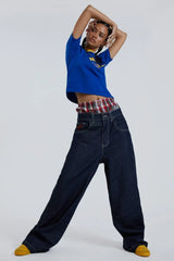 Woman posing in dark wash wide leg jeans with plaid waistband detail and a blue t-shirt with yellow stripes
