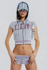 Model wearing a gray cropped zip-up hoodie with short sleeves and sequin embellishments on the front, accessorized with a denim cap and sunglasses.