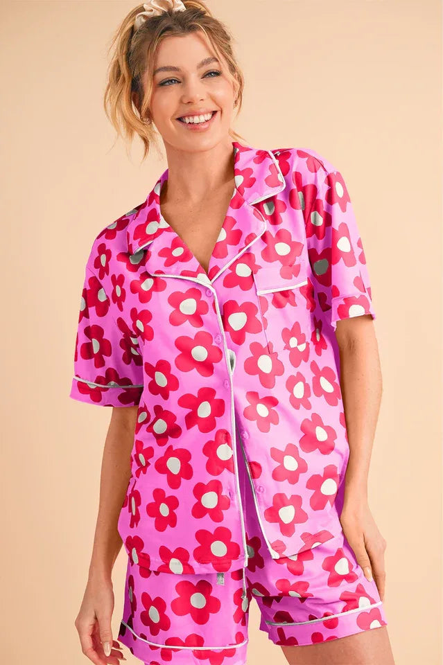 Woman wearing a bright pink floral print pajama set with red flowers and white piping.