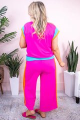 Woman wearing a bright pink two-piece set with blue and orange accents, standing indoors, back view.