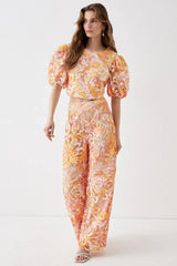 Model wearing a two-piece set with a cropped top and wide-leg pants featuring a floral lace overlay in orange, pink, and yellow.
