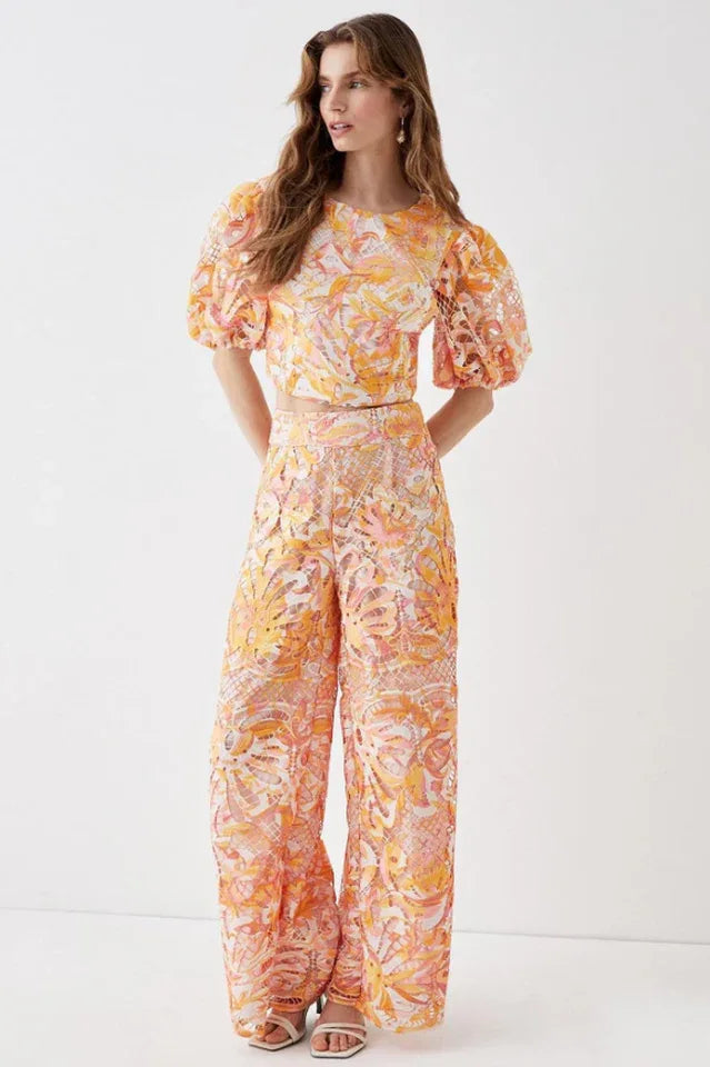 Full-length view of a model in an orange, pink, and yellow floral lace two-piece set.