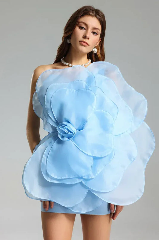 Woman wearing a light blue one-shoulder mini dress with a large floral appliqué on the bodice.