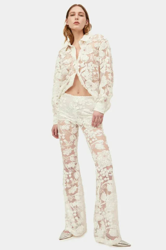 Woman wearing a sheer white lace button-down shirt and flare leg pants.