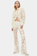 Woman wearing a sheer white lace button-down shirt and flare leg pants.