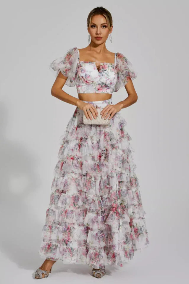 Woman in a white floral print two-piece set with a crop top and tiered maxi skirt.