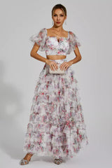 Woman in a white floral print two-piece set with a crop top and tiered maxi skirt.