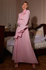 Woman posing in a pink maxi dress with a bow neck and flared sleeves, showcasing the draped fabric.