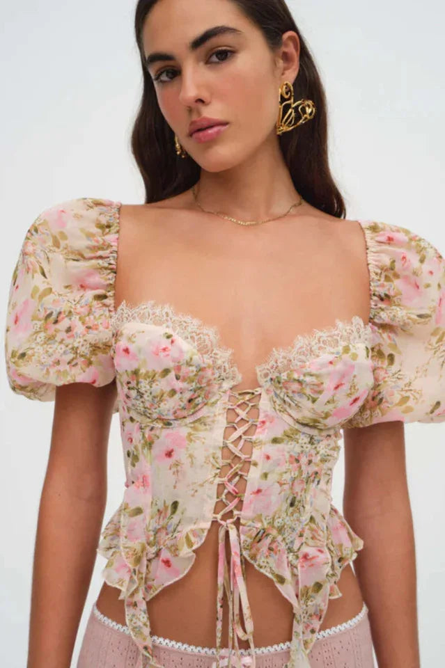 Close-up of a woman wearing a floral print corset top with puffy sleeves and a lace-up front.