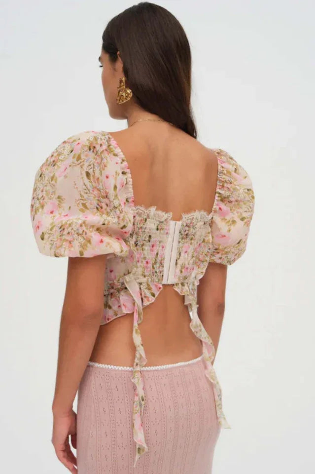 Back view of a woman wearing a floral print corset top with puffy sleeves and a lace-up front.