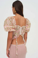 Back view of a woman wearing a floral print corset top with puffy sleeves and a lace-up front.