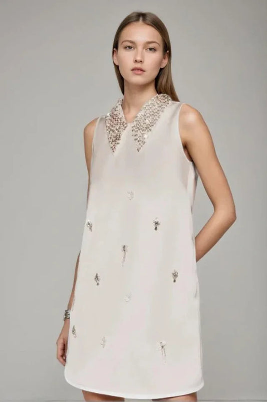 Model wearing a sleeveless ivory A-line mini dress with a heavily embellished pointed collar and scattered embellishments on the skirt.