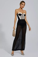 Woman wearing a strapless corset dress with a sheer black maxi skirt and holding a beige woven handbag.